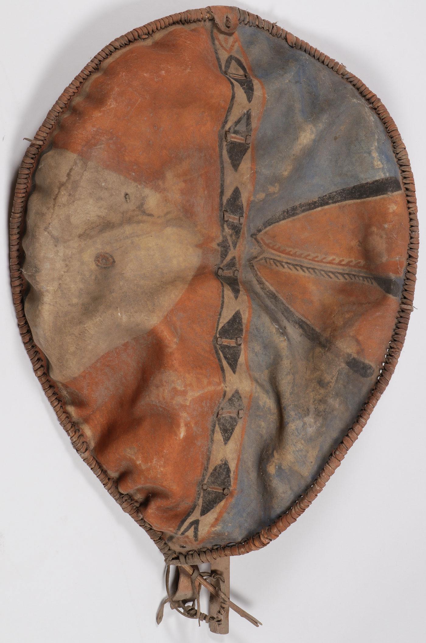AN AFRICAN HIDE SHIELD, MASAI, KENYA,: AN AFRICAN HIDE SHIELD, MASAI, KENYA, . Of traditional elliptical form with large carved wooden vertical bow-style handle and stretcher, and with hide wrapped hoop or band, the surface with polychrome