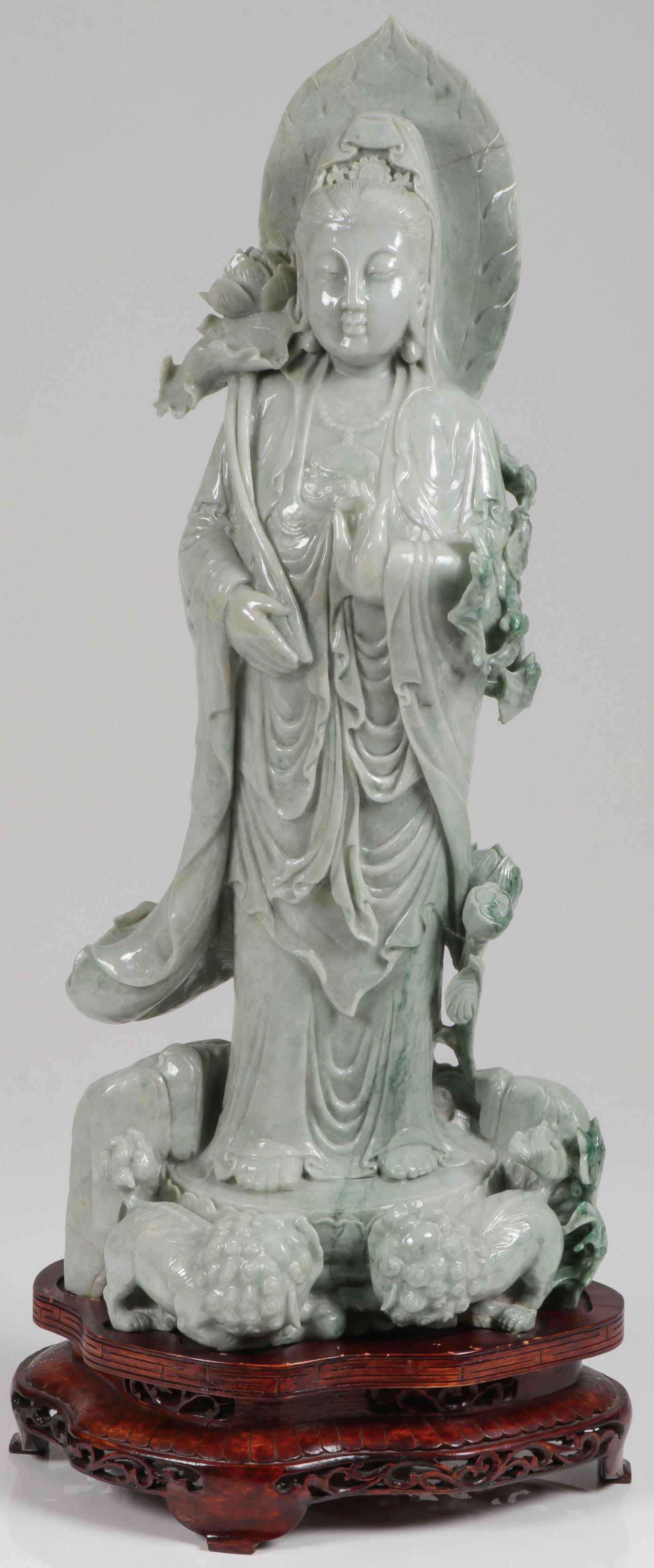 A CHINESE CARVED JADE FIGURE OF KWAN YIN: A CHINESE CARVED JADE FIGURE OF KWAN YIN. Finely carved in full round, shown standing on a lotus base with foo dogs and holding a floral scepter and resting on a carved wood stand. Height (excluding s