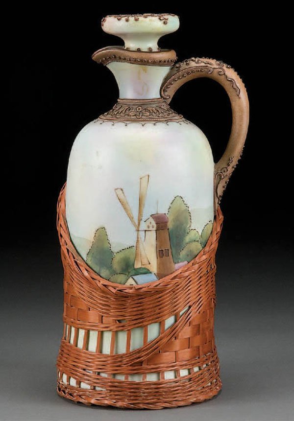NIPPON PORCELAIN & WICKER OVERLAY WINE JUG: A HAND PAINTED NIPPON PORCELAIN & WICKER OVERLAY WINE JUG with windmill scene below a moriage handle and neck. Blue maple leaf mark. Height 10.75 inches. Estimate $800-$1,200 Reference: The actual pie
