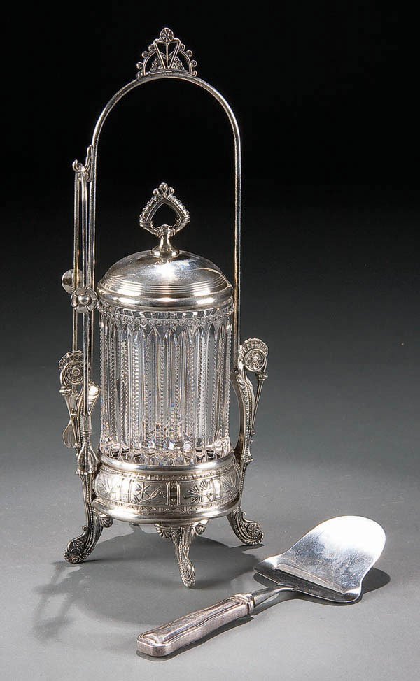 A VERY FINE VICTORIAN PAIRPOINT PICKLE CASTOR. La: A VERY FINE VICTORIAN PAIRPOINT PICKLE CASTOR. Late 19th Century, with beaded rib glass insert together with a Georg Jensen sterling cheese slicer. Height 13.25". Estimate $200-$400.