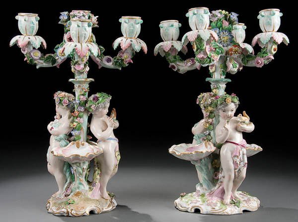 A DRESDEN STYLE PORCELAIN FIGURAL CANDELABRA PAIR: A DRESDEN STYLE PORCELAIN FIGURAL CANDELABRA PAIR 20th Century with figural putti under a four branch candle lamp with applied florals and hand painted decoration. Spurious blue crossed sword marks wi