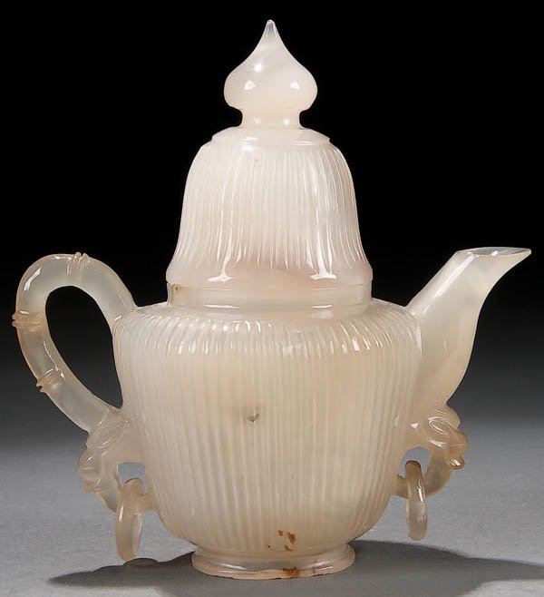 A FINE CHINESE CARVED AGATE LIDDED WINE POT 19th: A FINE CHINESE CARVED AGATE LIDDED WINE POT 19th century, Mughal style in translucent light tan agate with amber streaks. Free moving rings suspended from animal form masks. Height 4.75 inches (12 cm)
