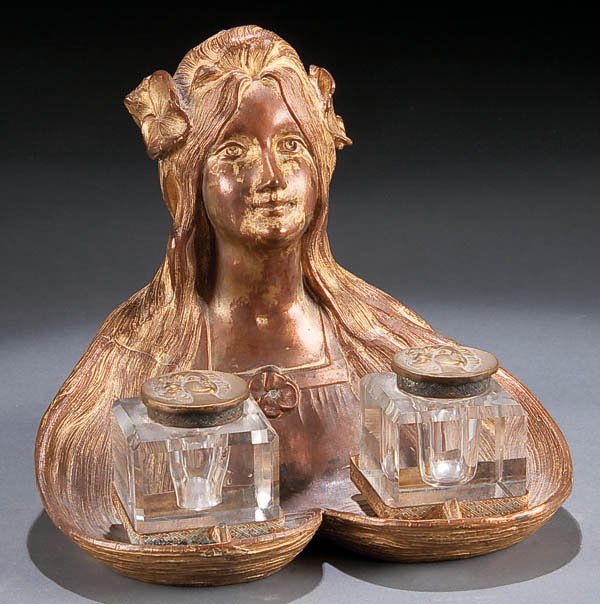 AN ART NOUVEAU ORMOLU DOUBLE INK WELL, circa 1900: AN ART NOUVEAU ORMOLU DOUBLE INK WELL, circa 1900, of a young beauty with flowing hair, encompassing two square cut glass wells with embossed facial form lids, height 7 inches. Estimate $100-$150