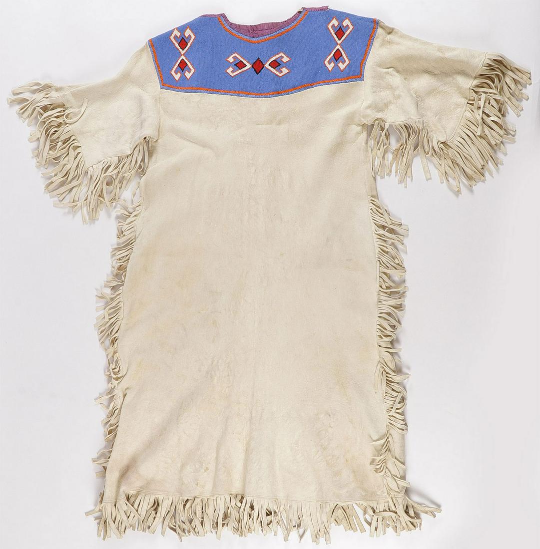 A BEADED PLAINS WOMAN'S DRESS: A BEADED PLAINS WOMAN'S DRESS. Comprising a soft brain tanned hide with fringe edging and beaded collar. Height 45 inches, width 47 inches. SHIPPING NOTICE: Jackson's is your sole and only source for