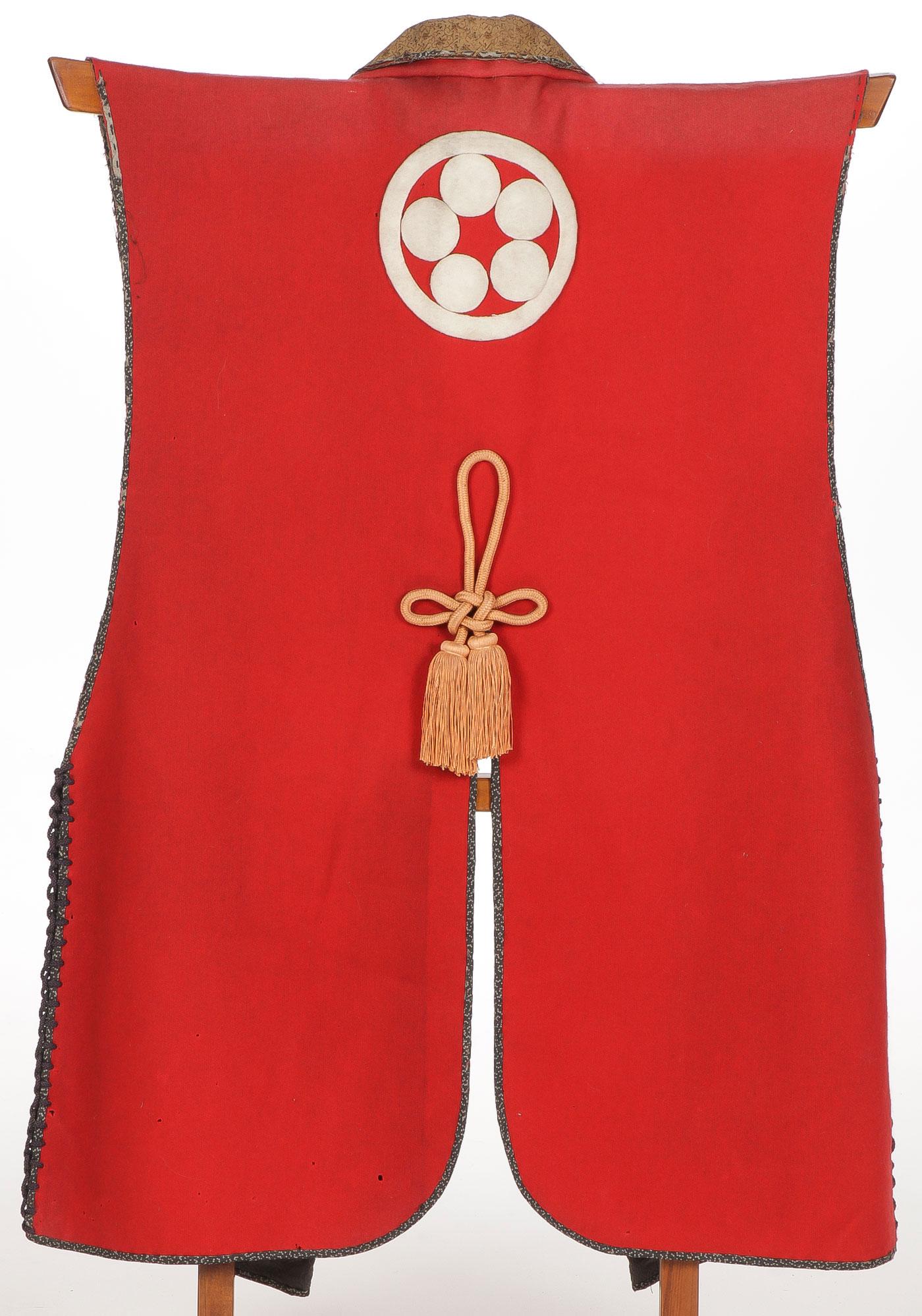 JAPANESE SAMURAI JINBAORI MEIJI: JAPANESE SAMURAI JINBAORI MEIJI. Comprising a traditional jinbaori surcoat of red wool body with decorative edging and thick felt mon on verso. Together with corresponding stand. Greatest width at sho