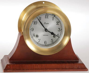 BOSTON SHIPSTRIKE BRASS CLOCK: BOSTON SHIPSTRIKE BRASS CLOCK. Comprising a brass cased ships bell clock by Chelsea clock company U.S.A. with 4-inch dial displaying Arabic numbers set on a conforming wooden stand.SHIPPING NOTICE:J