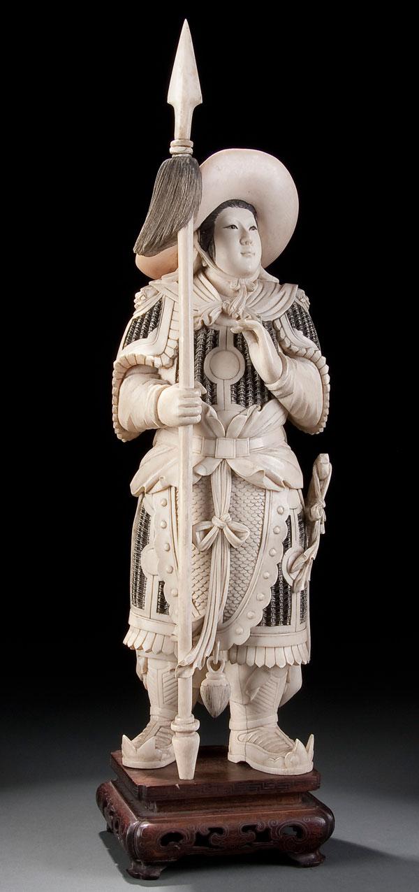 ORIENTAL CARVED IVORY FIGURE: A LARGE AND FINELY CARVED CHINESE IVORY FIGURE OF A WARRIOR early 20th century. Shown depicted in full armor with sword and spear, raised on a carved wood base. Total height 17.5 inches (44.5 cm).