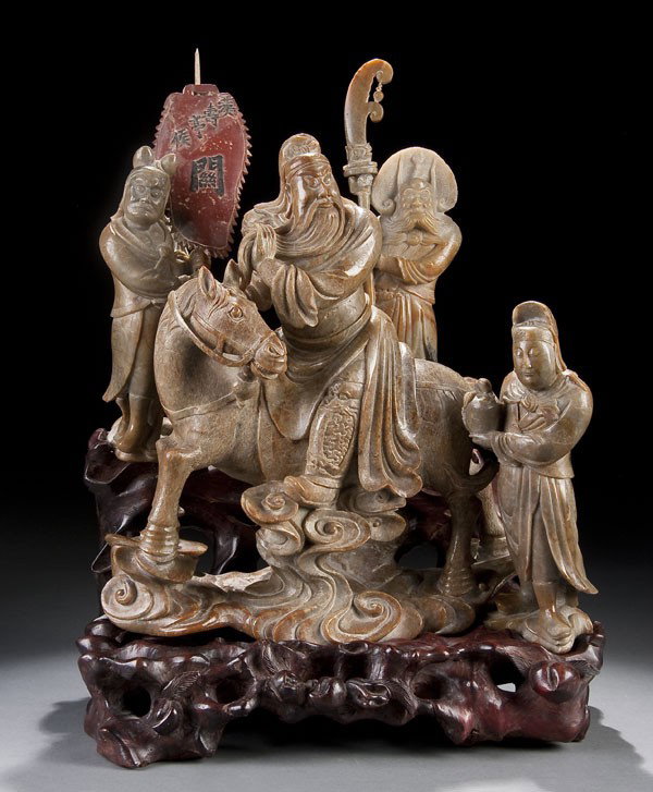 CHINESE CARVED SOAPSTONE FIGURAL GROUPING: A CHINESE CARVED SOAPSTONE FIGURAL GROUPING depicting a figure on horse with three attendants raised on a carved wooden stand. Total height 13 inches.