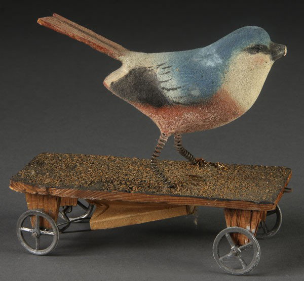 GERMAN SINGING BIRD PENNY PULL TOY: A GERMAN SINGING BIRD PENNY PULL TOY late 19th century. Wood and composition. Minor loss to beak. Length 4.75 inches. Contained in a later glass case (Not illustrated).