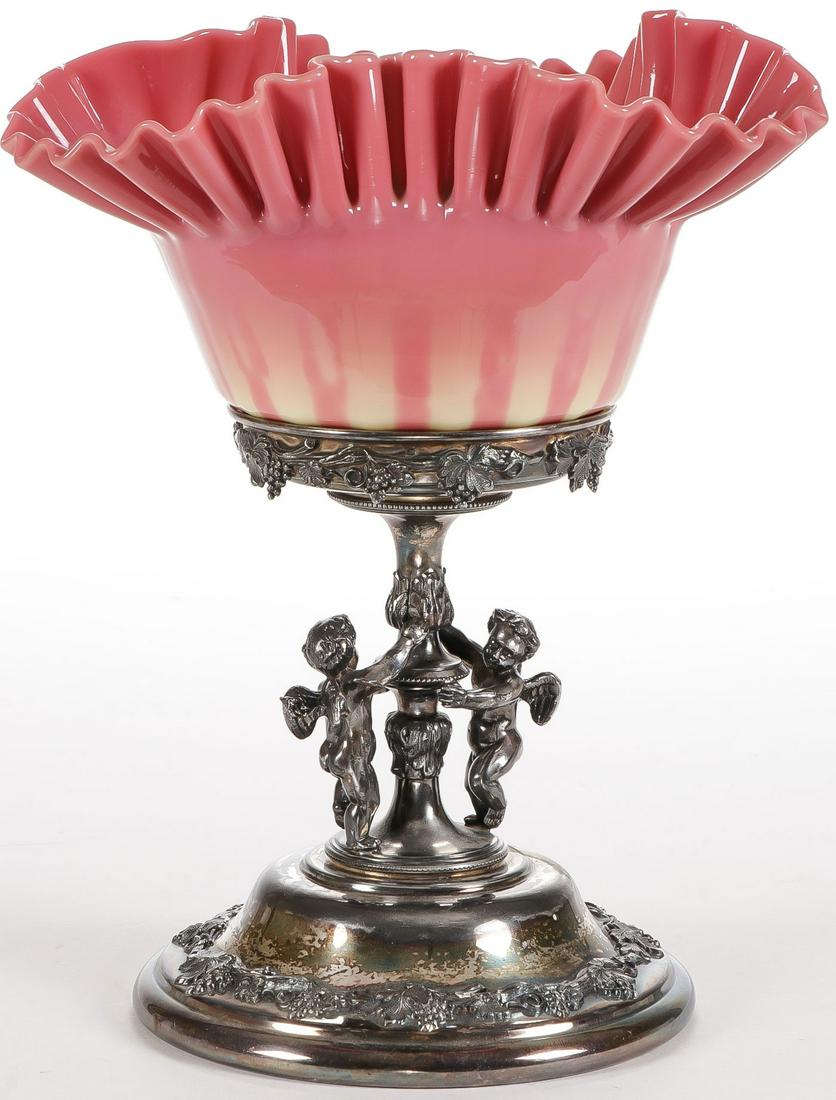 CASED GLASS CENTER BOWL AND STAND C. 1890: CASED GLASS CENTER BOWL AND STAND C. 1890. Comprising a Forbes silver plated stand comprising two winged putti supporting a central stem with overhanging grape banding holding a Burmese cased glass st