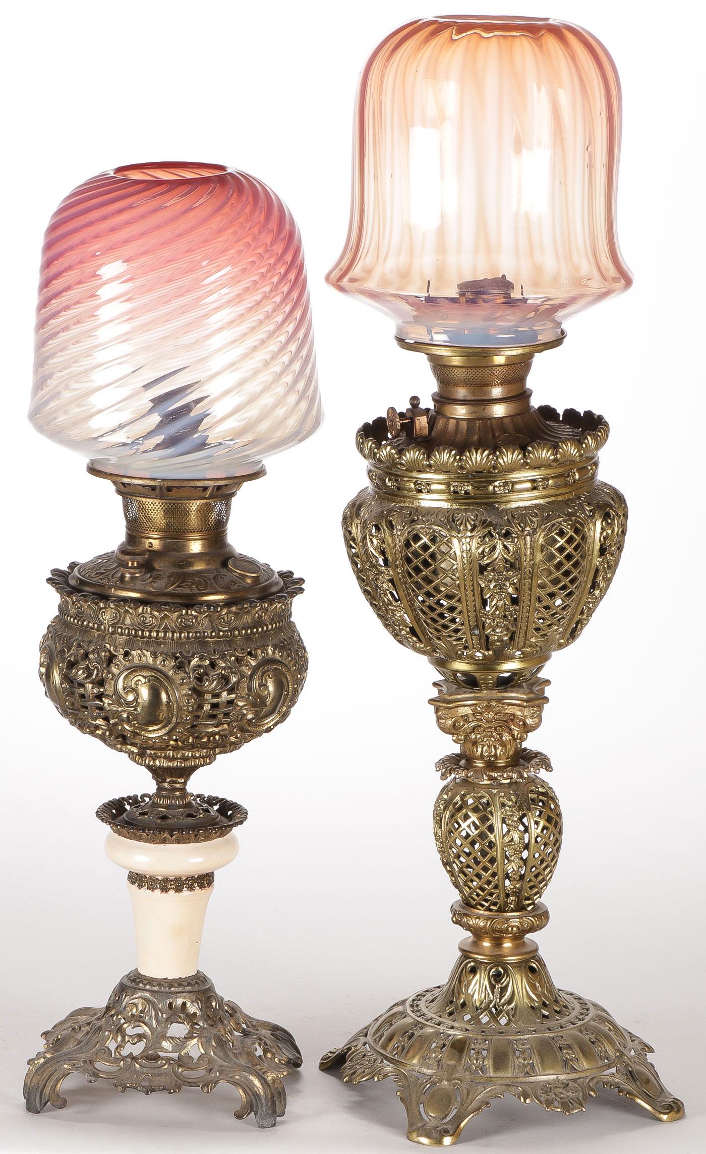 PAIR VICTORIAN BANQUET LAMPS: PAIR VICTORIAN BANQUET LAMPS. Comprising a pair of ornate pierced brass lamp bases, each with original oil font. One with swirl glass shade, the other with a ribbed bell-shaped shade. Heights 27.5 inc