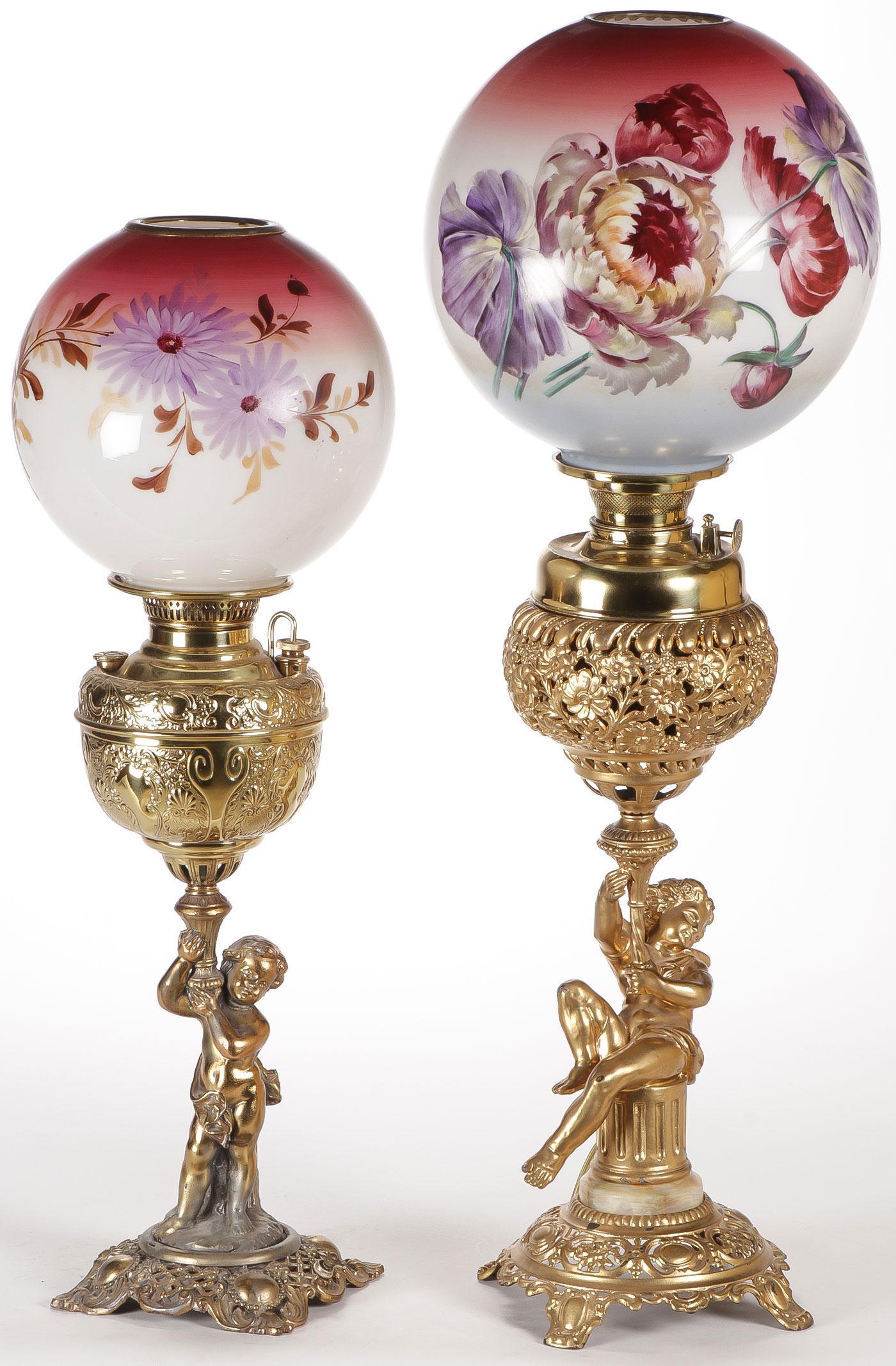PAIR VICTORIAN FIGURAL BANQUET LAMPS 19TH C: PAIR VICTORIAN FIGURAL BANQUET LAMPS 19TH C. The base of each mounted with putti beneath a font, both with hand-painted shades. The smaller of the two electrified. Heights 31.5 inches and 27 inches. S