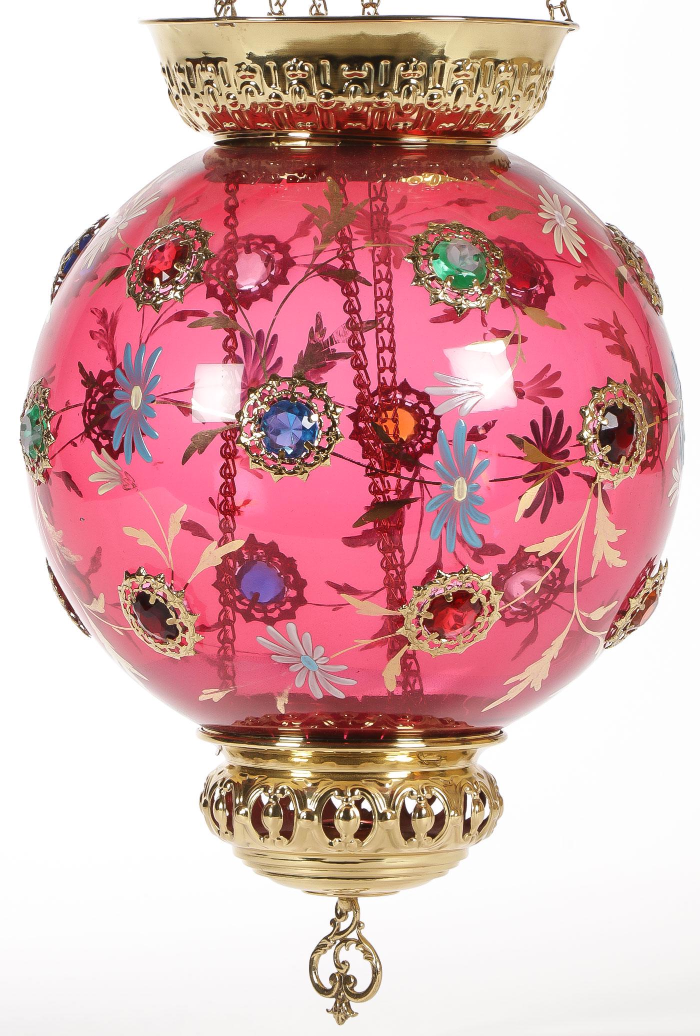 CRANBERRY JEWELED HANGING PARLOR LAMP: CRANBERRY JEWELED HANGING PARLOR LAMP. The cranberry globe shade set with 18 various jewels and hand-enameled with flowers and gilt scrolling foliage. Height from smoke bell to base 34 inches. Diamete