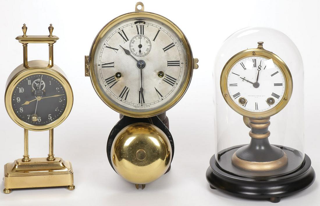 VINTAGE CLOCK GROUP: VINTAGE CLOCK GROUP. Comprising an American brass wall mounted alarm clock, a Vance & Mitchell pedestal pendulum clock under glass dome and a British brass desk clock. Greatest height 11 inches. SHIPP
