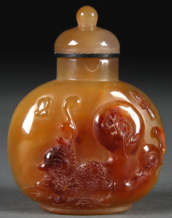 2 CHINESE CARVED AGATE SNUFF BOTTLES, 20TH C: A PAIR OF CHINESE CARVED AGATE SNUFF BOTTLES, 20TH CENTURY, in smoky amber colored stone with reddish brown highlights carved with a mythical beast and fungus and a mythical beast with bats. Height 3.