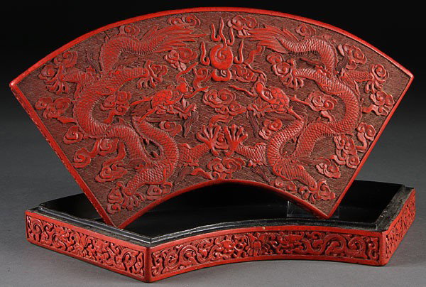 CHINESE CARVED CINNABAR DRAGON STORAGE BOX: A CHINESE CARVED CINNABAR DRAGON DECORATED SEMI-ROUND LIDDED STORAGE BOX, EARLY 20TH CENTURY, finely carved with two scrolling dragons and stylized clouds on an incised diaper ground with carved figur