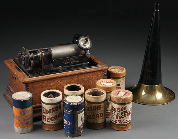 AN EDISON STANDARD PHONOGRAPH, CIRCA 1900. With : AN EDISON STANDARD PHONOGRAPH, CIRCA 1900. With oak case and brass rimmed horn. Includes 12 cylinders (case top cover absent). Length 13 inches.
