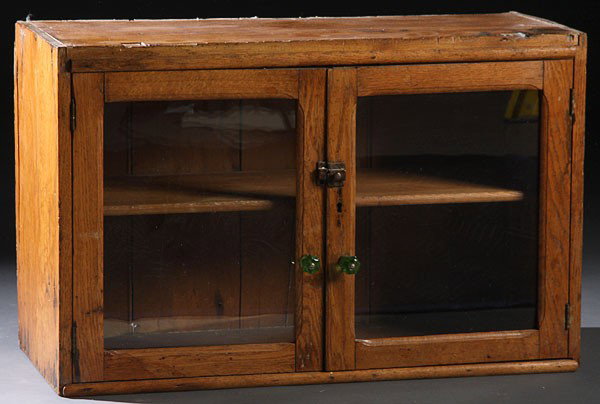 PRIMITIVE 19TH C OAK WALL HANGING CUPBOARD: A PRIMITIVE 19TH CENTURY OAK WALL HANGING CUPBOARD, with two glazed doors and green depression glass pulls. Height 20 inches, width 32 inches, depth 13.25 inches.