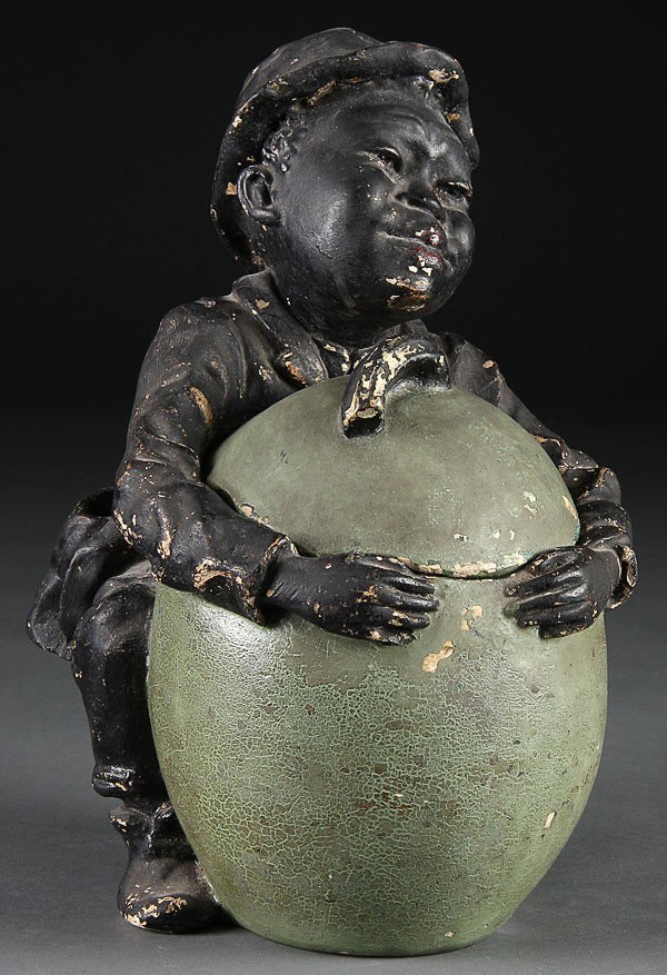 A BLACK AMERICANA BOY WITH WATERMELON HUMIDOR, CI: A BLACK AMERICANA BOY WITH WATERMELON HUMIDOR, CIRCA 1900. Polychrome cast plaster. Height 11 inches.