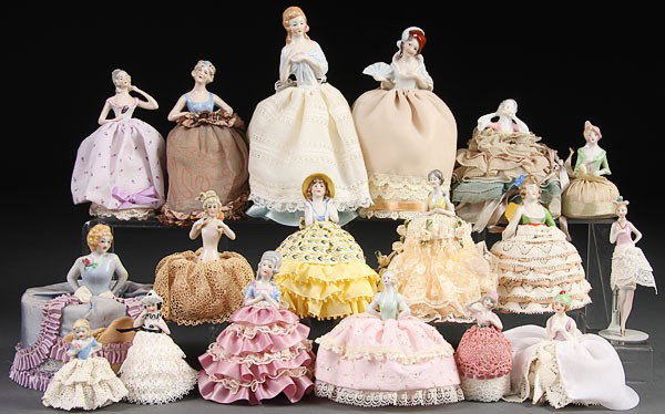 A COLLECTION OF 17 PORCELAIN HALF DOLL PIN CUSHIO: A COLLECTION OF 17 PORCELAIN HALF DOLL PIN CUSHIONS, EARLY 20TH CENTURY. Mostly German, depicting women in various pose including holding a fan and a nude holding a hand mirror, one with crossed legs.