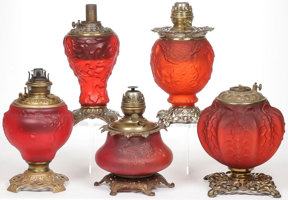 RED SATIN GLASS KEROSENE LAMPS: RED SATIN GLASS KEROSENE LAMPS. Comprising five vintage red satin glass kerosene lamp bases as shown, including a cupid kissing a woman. Probably Consolidated. No shades, sold as shown. Greatest heigh