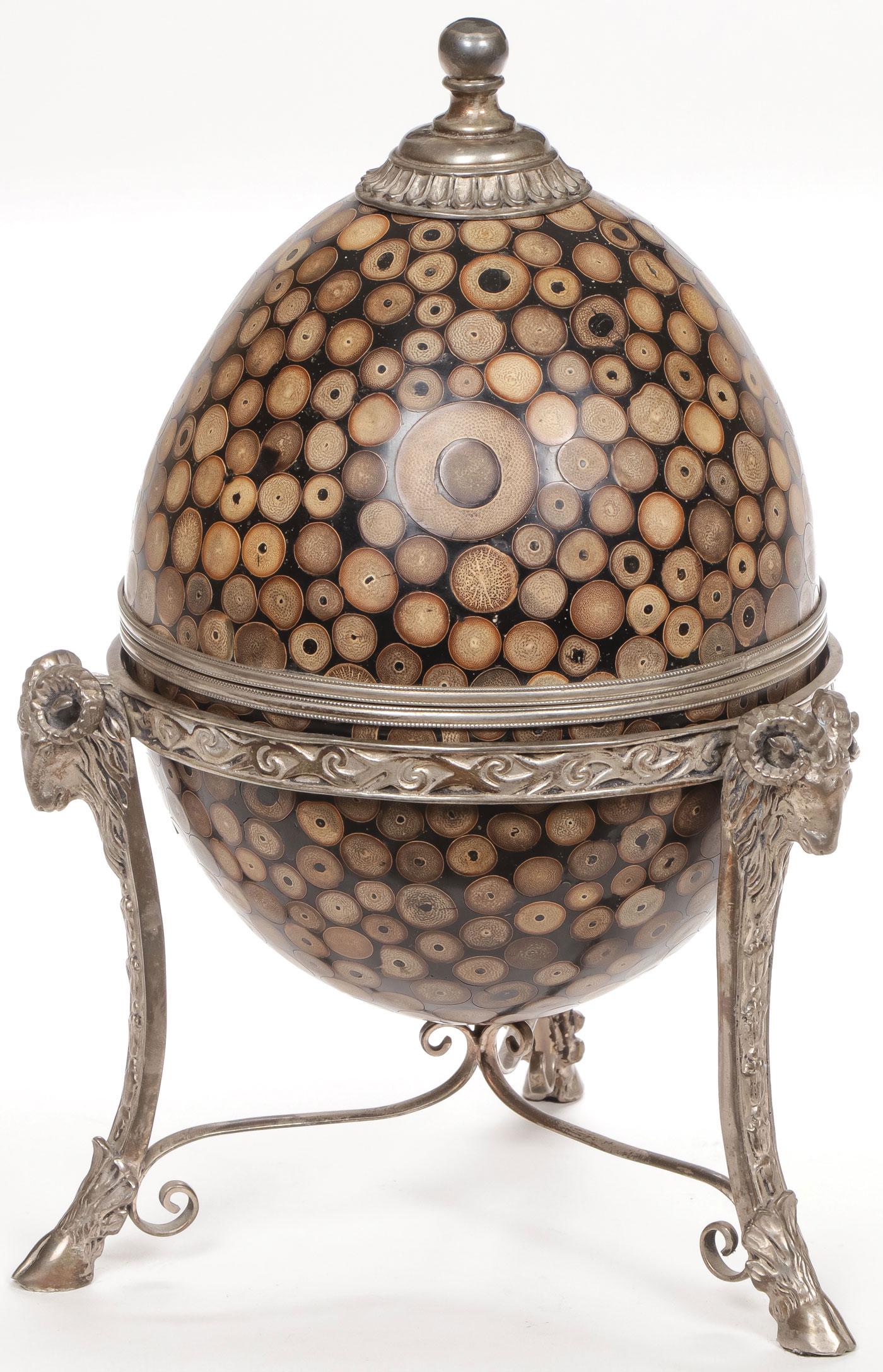 A CUT BAMBOO EGG FORM BOX: A CUT BAMBOO EGG FORM BOX. Comprising a two-piece egg made of composite cut and polished bamboo with German silver mounts and resting in an ornate silver-plated stand with rams' heads terminating with