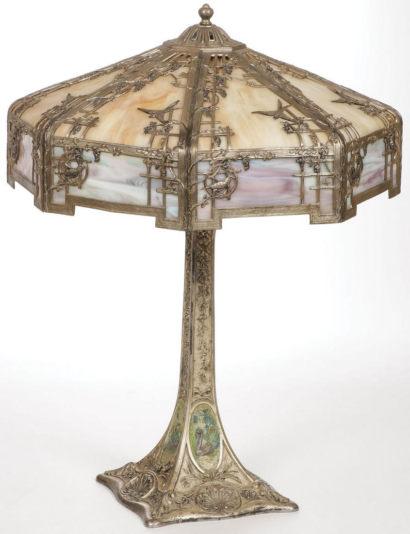 AN IMPRESSIVE SLAG GLASS LAMP C. 1920'S: AN IMPRESSIVE SLAG GLASS LAMP C. 1920'S. Comprising a large table lamp of octagonal form set with brown, purple, and blue slag glass with ornate metal overlay depicting vines and doves set on an intri