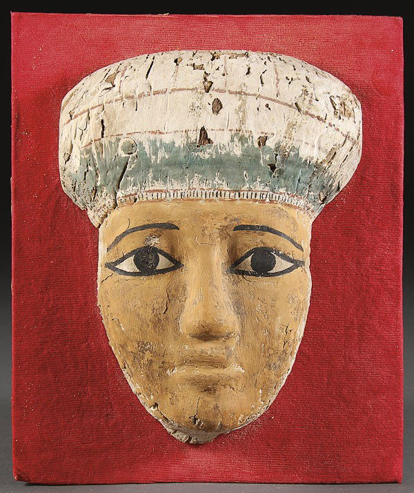 AN EGYPTIAN POLYCHROME SARCOPHAGUS FUNERARY MASK: AN EGYPTIAN POLYCHROME SARCOPHAGUS FUNERARY MASK. Probably Dynastic period, with green, white and amber pigments over plaster and carved wood. Some minor losses. Height 10 inches.