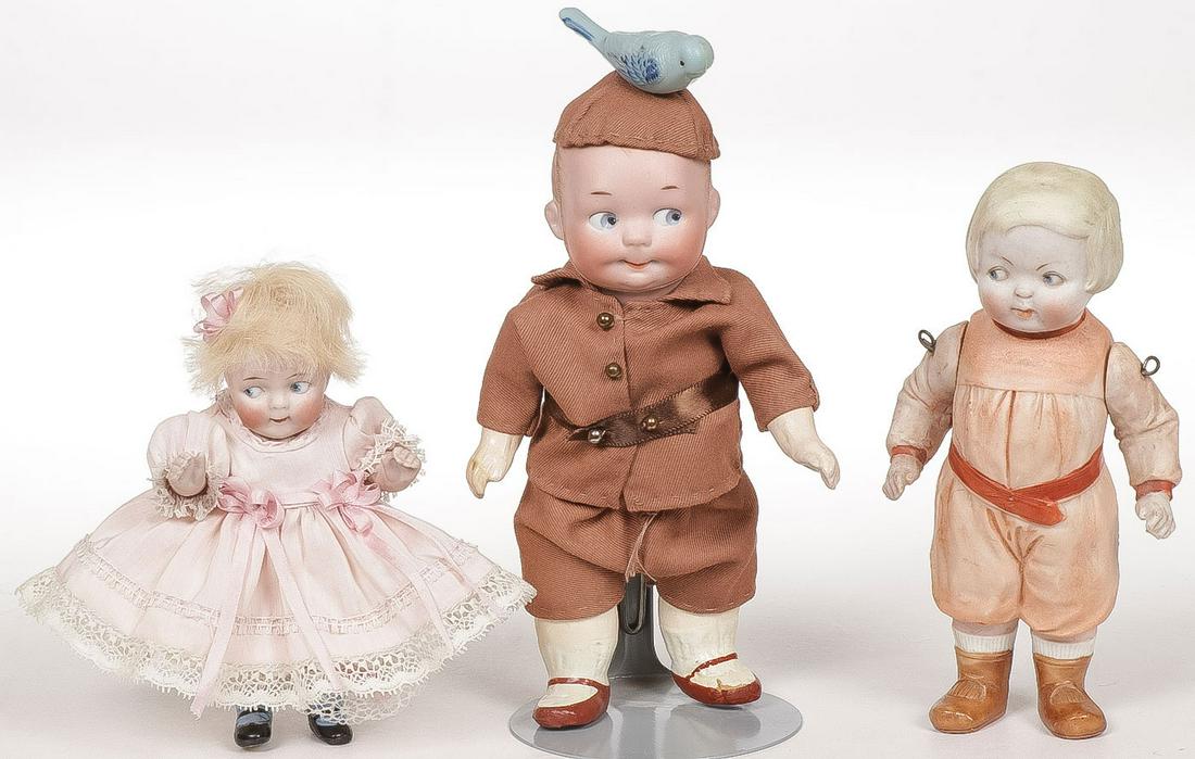THREE CHARMING BISQUE GOOGLY DOLLS: THREE CHARMING BISQUE GOOGLY DOLLS. Including a Googly boy with five-piece chunky compo body and brown suit with bluebird cap, an all-bisque jointed Googly girl with watermelon mouth with small chip o