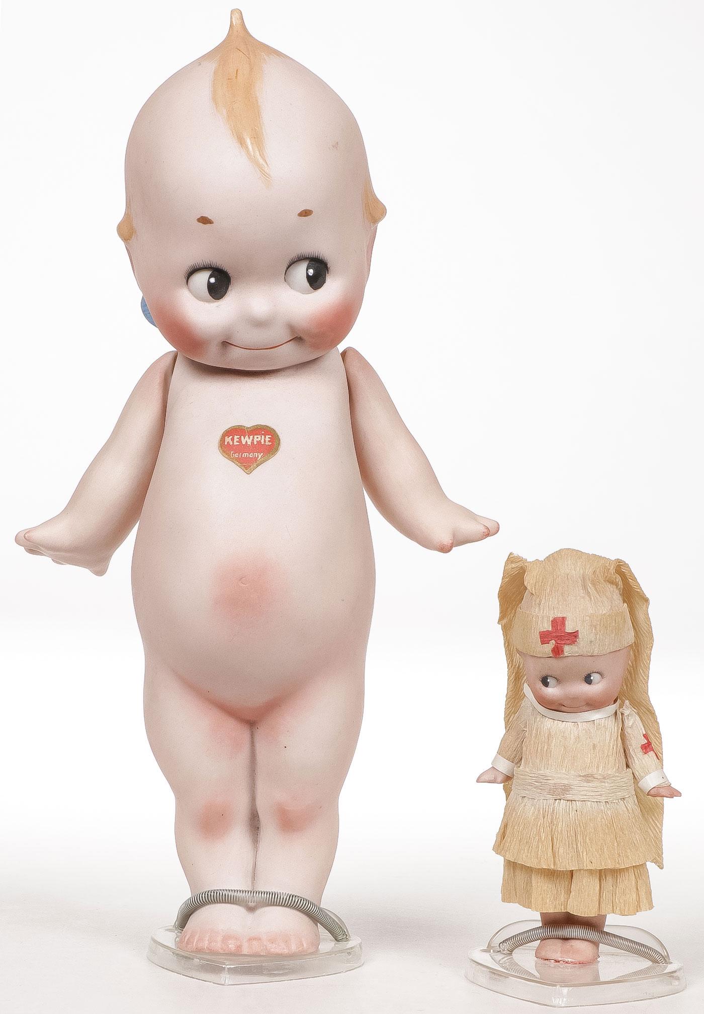 PAIR OF BISQUE KEWPIE DOLLS: PAIR OF BISQUE KEWPIE DOLLS. Comprising a large example of traditional form with original heart logo on chest, height 10.5 inches, and a WWI period nurse with crepe paper Red Cross nurses' uniform.SHI