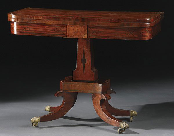 EMPIRE MAHOGANY GAME TABLE POSSIBLY RUSSIAN: AN EMPIRE GILT BRONZE MOUNTED MAHOGANY INLAID GAME TABLE, POSSIBLY RUSSIAN. The folding rectangular top with inlaid bronze border raised on an ebony inlaid pedestal above modified "C" scroll legs term