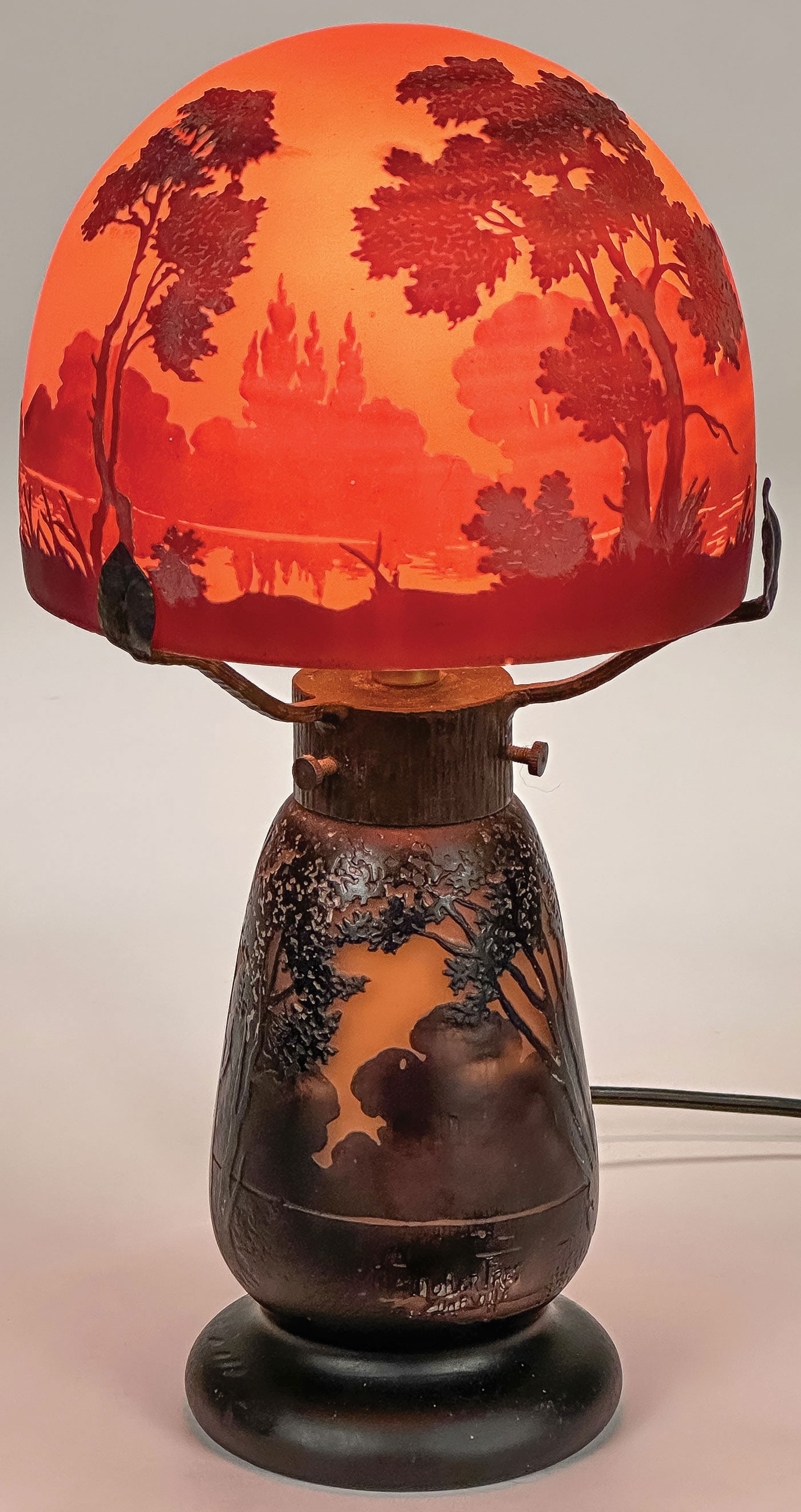 MULLER FRES CAMEO GLASS LAMP: MULLER FRES CAMEO GLASS LAMP In two pieces with wrought iron frame supporting a mushroom domed shade depicting a dusk landscape, signed on base and shade Muller Fres Luneville. Height 12 inches (30.5c
