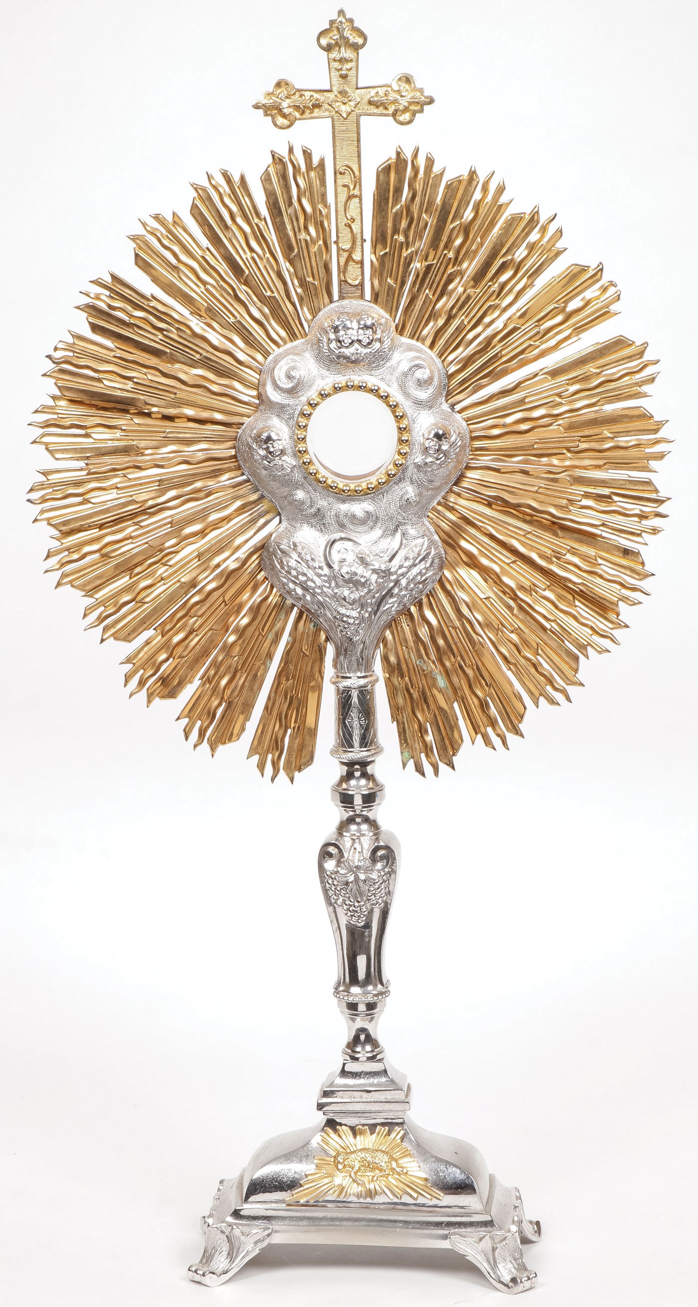 A SILVER GILT MONSTRANCE 19TH C: A SILVER GILT MONSTRANCE 19TH C. Resting on scroll paw feet the base with the Angus Dei with wheat and grape motif silvered exposition window decorated with chased clouds and winged cherubs and ornate