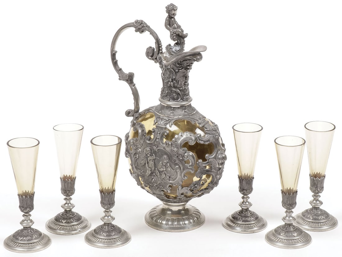 A GERMAN 8-PIECE PEWTER AND GLASS WINE SET, 19TH: A GERMAN 8-PIECE PEWTER AND GLASS WINE SET, 19TH C. Comprising an amber colored decanter set in an ornate pewter frame with large scroll handle and bacchanal putti finial. Together with six matching a