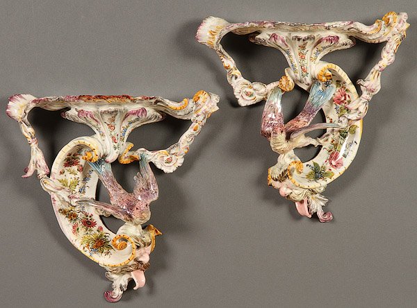 ITALIAN FAIENCE POTTERY , 18TH CENTURY: A PAIR OF ITALIAN FAIENCE ROCOCO STYLE POTTERY WALL BRACKETS, 18TH CENTURY. With large C scrolls suspended by foliate garlands containing a figural wing spread bird, sun mark with letter E on verso, s