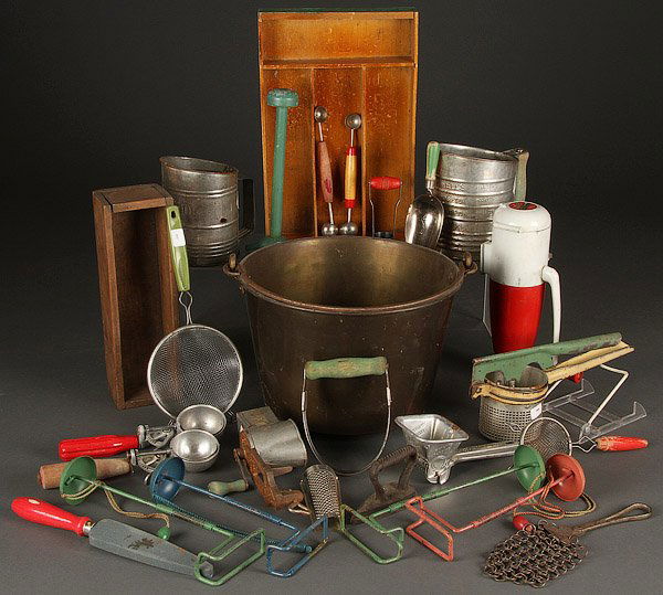 A PRIMITIVE KITCHEN UTENSIL COLLECTION: A PRIMITIVE KITCHEN UTENSIL COLLECTION. Over 20 pieces including red and green handled wood utensils, red and white rocket shaped ice crusher, flour sifters, graters, a large brass pail and other ite