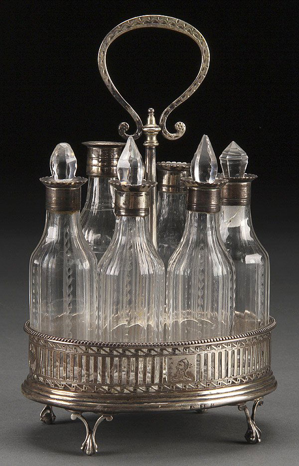 A GEORGE III SILVER AND CUT GLASS CASTOR SET: A GEORGE III SILVER AND CUT GLASS CASTOR SET, LONDON, CIRCA 1804. Possibly by Thomas Holland, the mahogany base with pierced silver gallery raised on claw and ball feet below a center handle with harp