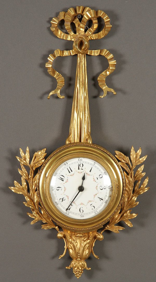 A FRENCH NAPOLEON III GILT BRONZE WALL CLOCK: A FRENCH NAPOLEON III GILT BRONZE WALL CLOCK, LATE 19TH CENTURY. With enameled dial within a circular case suspended from a tied ribbon form, later electrified. Length 25 inches (63.5 cm).