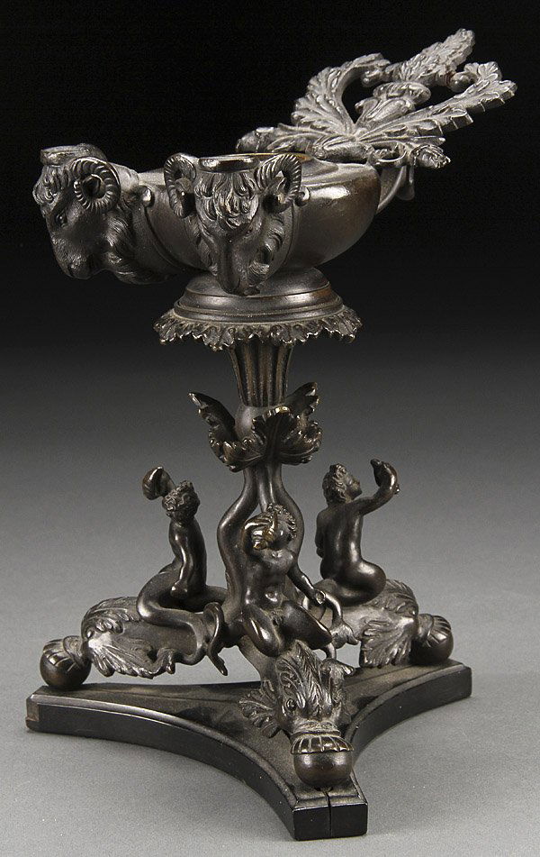NEOCLASSIC BRONZE OIL LAMP, CIRCA 1800 OR OLDER: A NEOCLASSIC BRONZE OIL LAMP,PROBABLY ITALIAN OR FRENCH CIRCA 1800 OR PERHAPS MUCH OLDER. The bronze oil font with scrolled foliate handle and two figural ram's head wick spouts raised on three legged