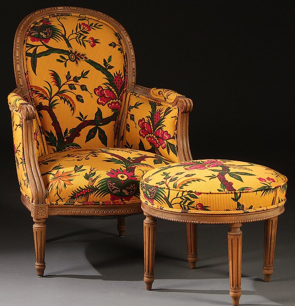 A LOUIS XVI STYLE CARVED WALNUT ARM CHAIR: A LOUIS XVI STYLE CARVED WALNUT ARM CHAIR, EARLY 20TH CENTURY. With matching round ottoman and later Chinoiserie floral print upholstery. Height 37.5 inches (95.2 cm).