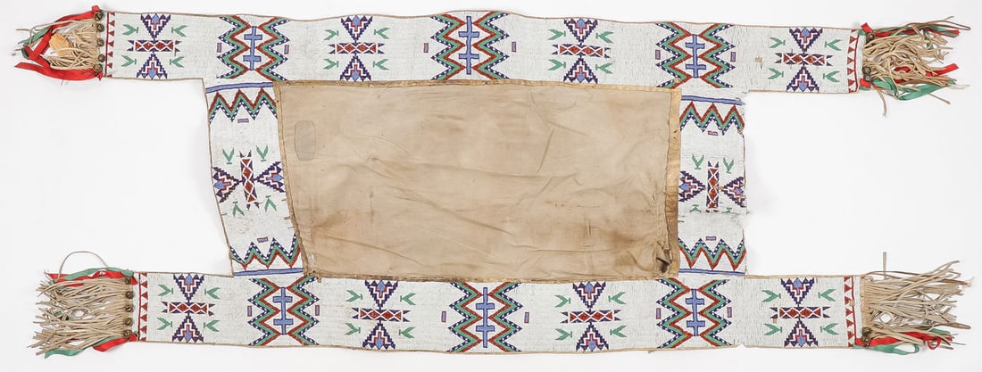 A SIOUX BEADED SADDLE BLANKET, C. 1900: A SIOUX BEADED SADDLE BLANKET, C. 1900. Of traditional design, lazy stitch, sinew-sewn on hide. Finely beaded with traditional geometric designs and fringe, silk ribbon, and bell drops. 77 inches x 27