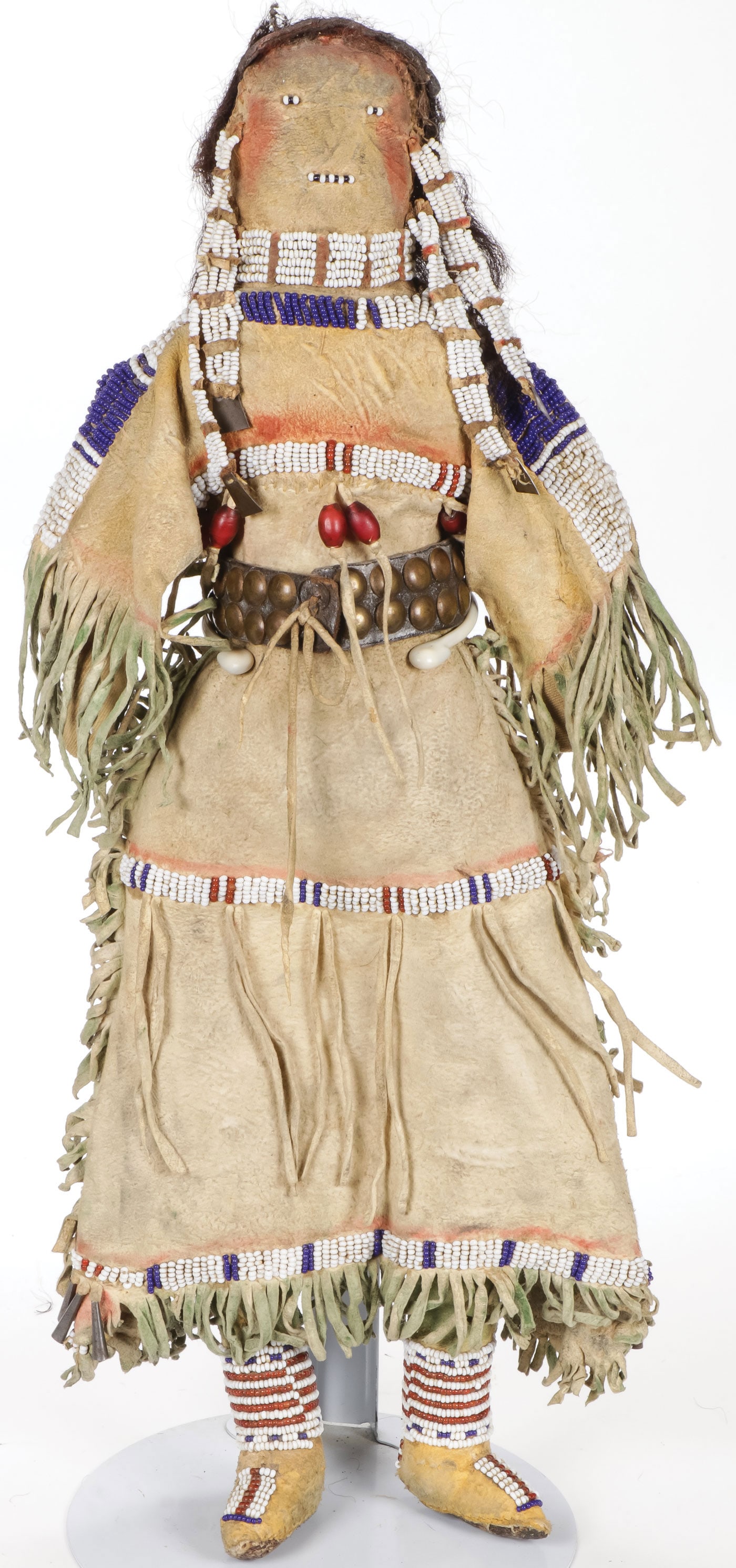 A GOOD CHEYENNE BEADED HIDE DOLL, C.1900: A GOOD CHEYENNE BEADED HIDE DOLL, C.1900. Stuffed cotton body with tan hide, sinew-sewn and lazy-stitch beaded dress, leggings, and moccasins. Green tinted fringe with cone drops, brass tack belt, and