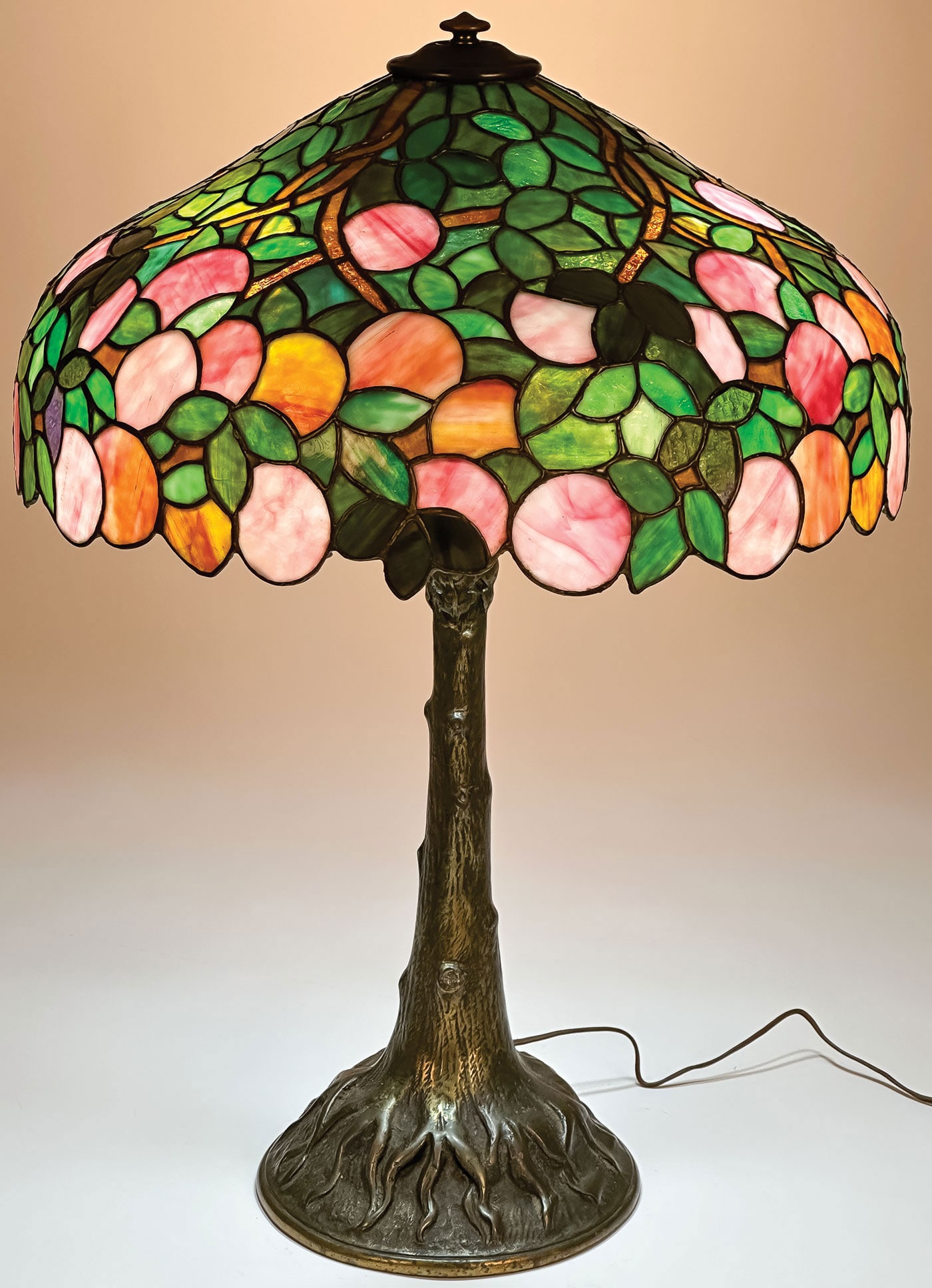 A CINCINNATI FRUIT TREE LEADED GLASS TABLE LAMP: A CINCINNATI FRUIT TREE LEADED GLASS TABLE LAMP, C. 1910. Comprising a Cincinnati Wrought Iron Works fruit or peach tree lamp. Patinated bronze tree form base with three light sockets and with peach t