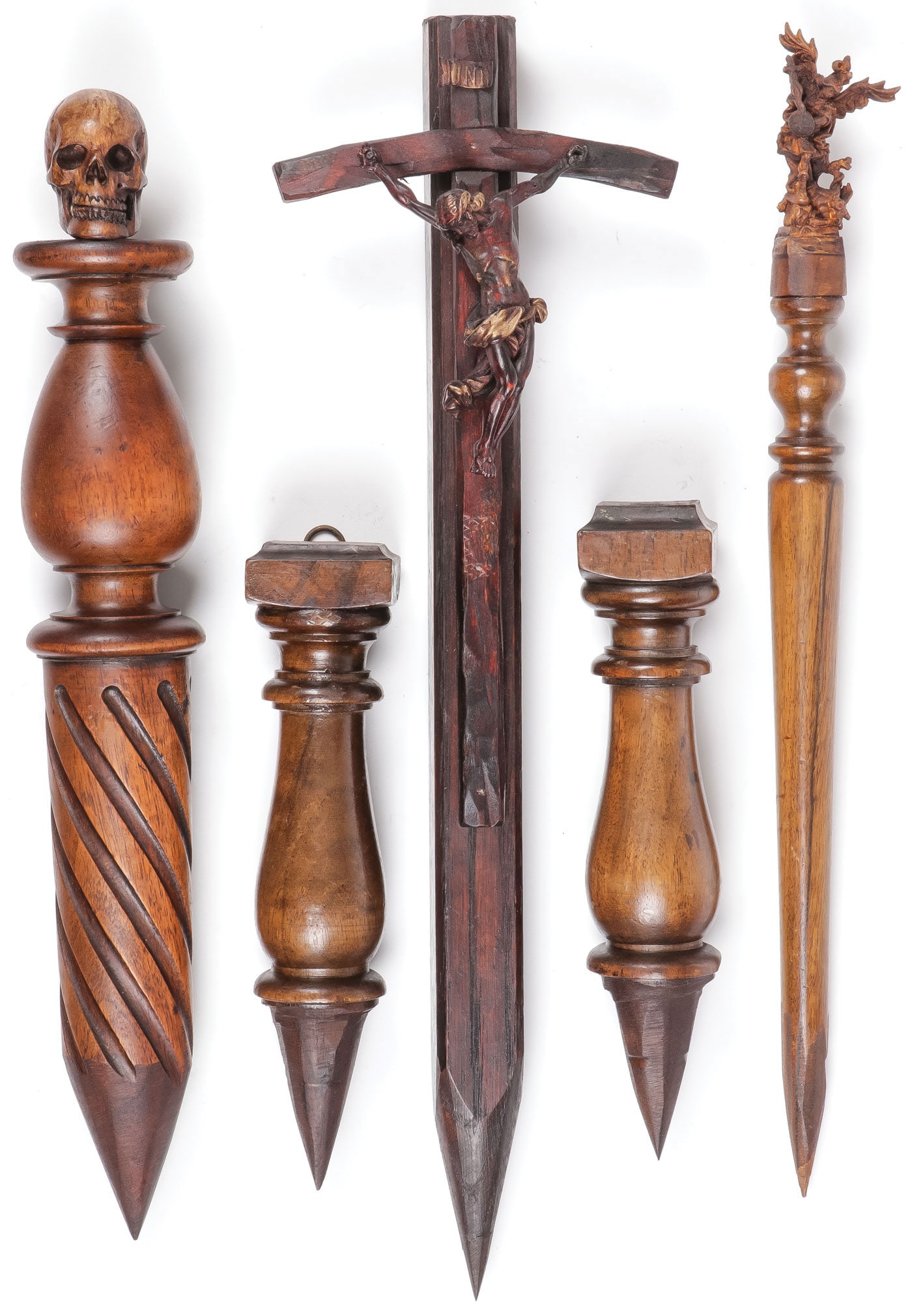 FIVE VAMPIRE KILLING WOOD STAKES: FIVE VAMPIRE KILLING WOOD STAKES. Of various shapes and sizes, the finial of one with carved skull (far left), another with the Archangel Michael (far right) a crucifix form example, and others, as sh