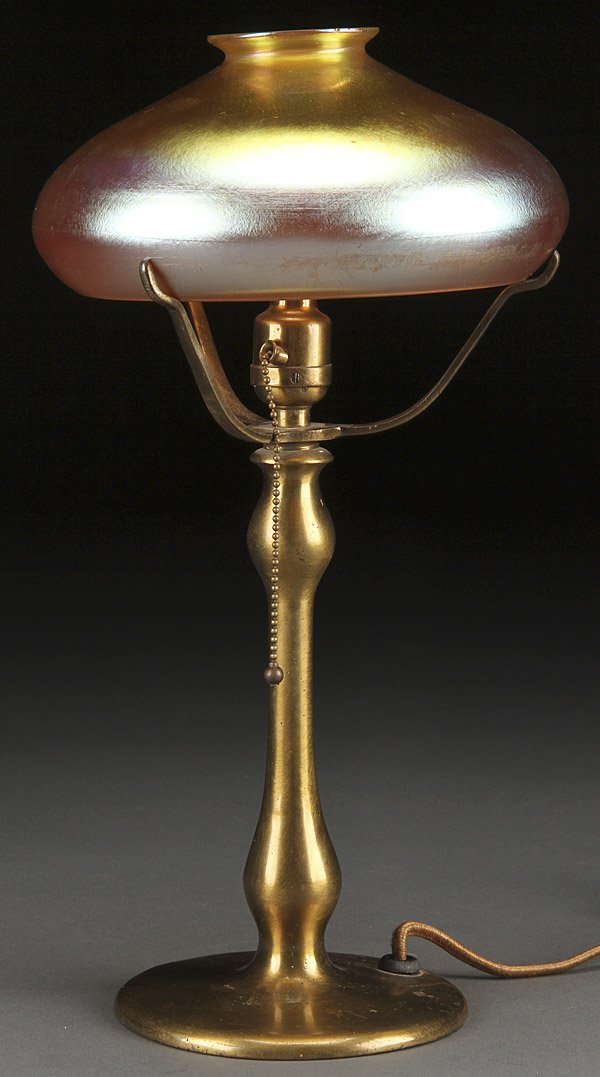 AN AMERICAN IRIDIZED GLASS & BRONZE TABLE LAMP: AN AMERICAN IRIDIZED GLASS AND BRONZE TABLE LAMP, CIRCA 1900. The iridized gold glass shade in the manner of Steuben with associated bronze baluster form base and hubble socket. Height 13 inches, diam