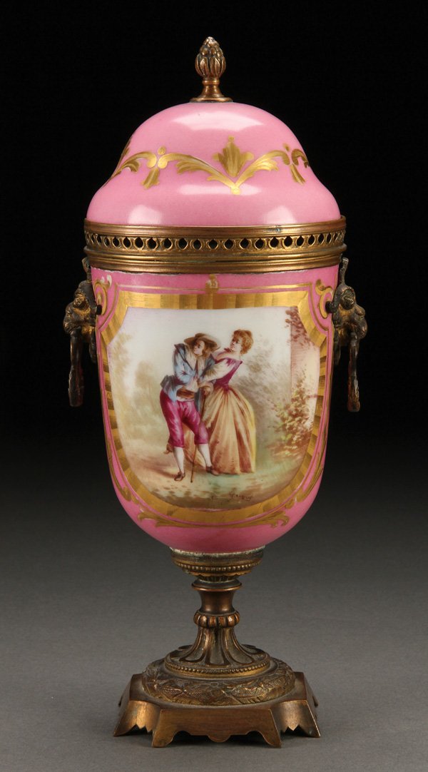 SEVRES STYLE PORCELAIN COVERED URN: A SEVRES STYLE HAND PAINTED PORCELAIN AND BRONZE MOUNTED COVERED URN, 19TH CENTURY. With romantic hand painted scene of a couple reserved on a pink ground flanking lions head handles, raised on a bron