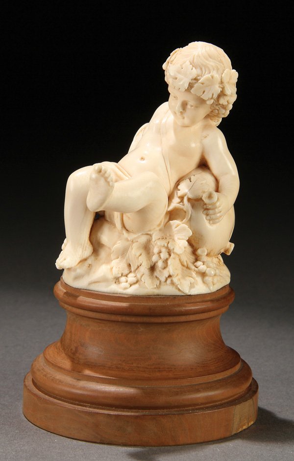 A GOOD FRENCH CARVED IVORY BACCHANALIAN INFANT: A GOOD FRENCH CARVED IVORY BACCHANALIAN INFANT, SIGNED CLOVIS DELACOUR (1859-1929). Fully carved in the round. Depicting a sleepy infant with wine cup resting atop a wineskin on grape cluster mound. I