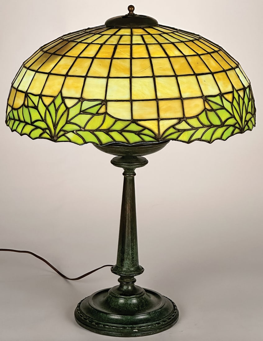 AN AMERICAN LEADED GLASS TABLE LAMP: AN AMERICAN LEADED GLASS TABLE LAMP. The rim of leaded shade trimmed with ivy leaves and overall in graduated geometric squares, possibly Lamb Brothers & Greene, resting on a finely crafted weighted b