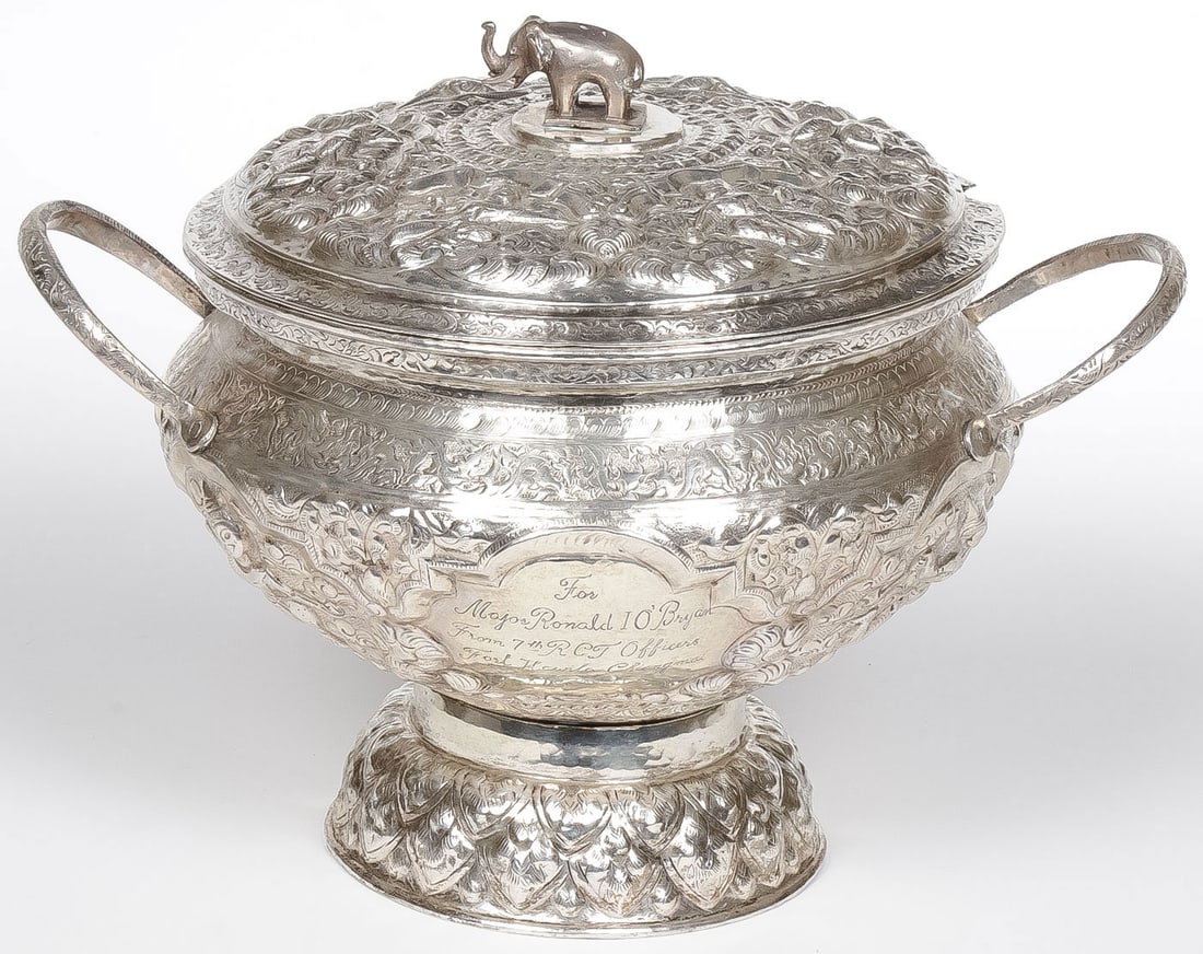 A THAI MILITARY PRESENTATION COVERED TUREEN: A THAI MILITARY PRESENTATION COVERED TUREEN. Comprising an ornate silver plated repousse covered tureen, the sides with engraved dedicatory inscription, "For Major Ronald I. O'Bryan from 7th RCT Offic