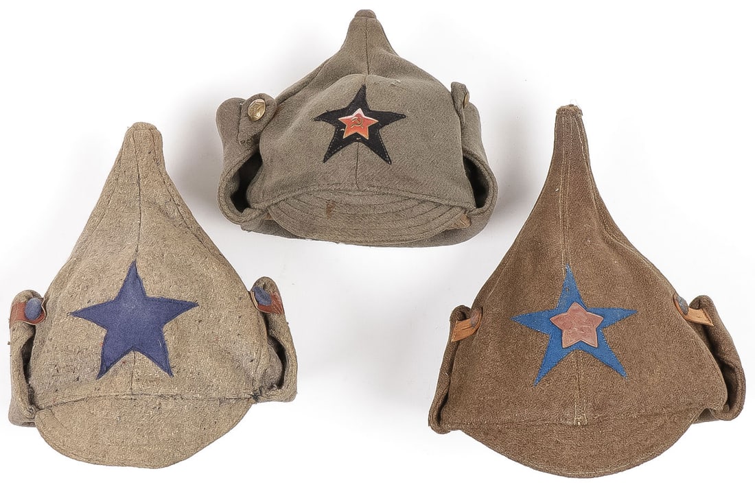THREE EARLY RUSSIAN BUDENOVKI, C. 1921-1935: THREE EARLY RUSSIAN BUDENOVKI, C. 1921-1935. Comprising a good transitional group of Budenovki, including an early pointed top in salt and pepper grey wool with artillery blue star, blue cloth covered